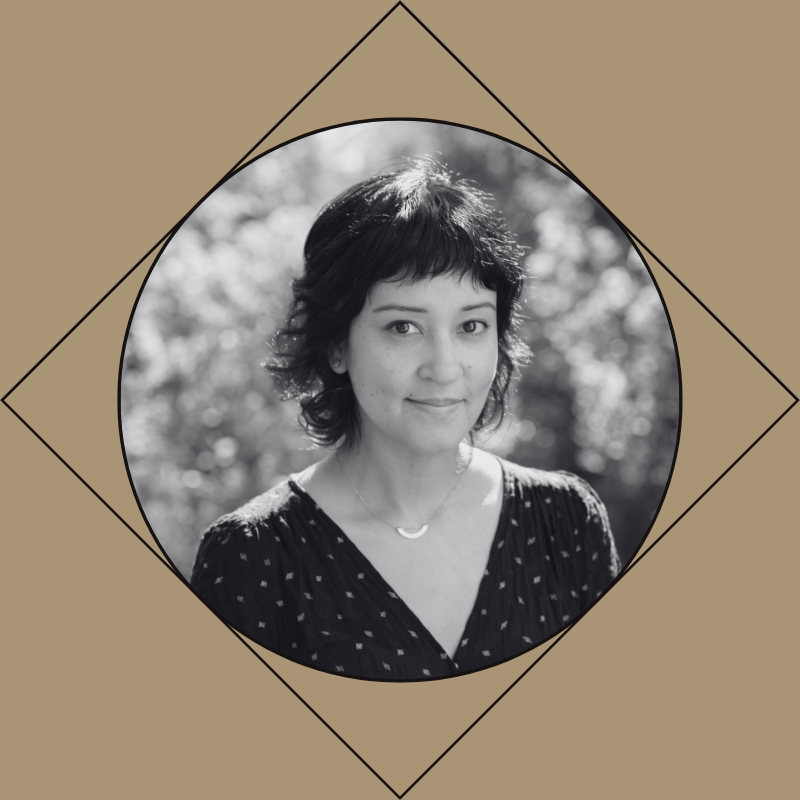Black and white portrait of a woman with short dark hair, wearing a patterned blouse and a delicate necklace, standing outdoors with blurred trees in the background.