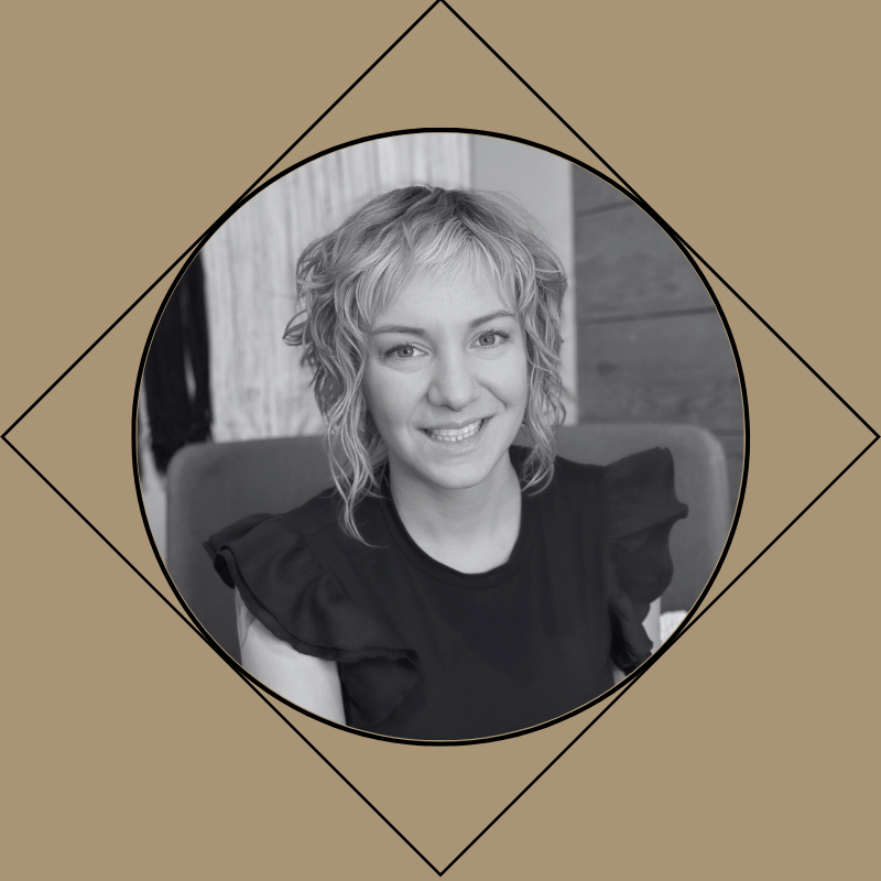 Black and white portrait of a young female hairstylist with curly short hair, smiling, wearing a black top with ruffled sleeves.