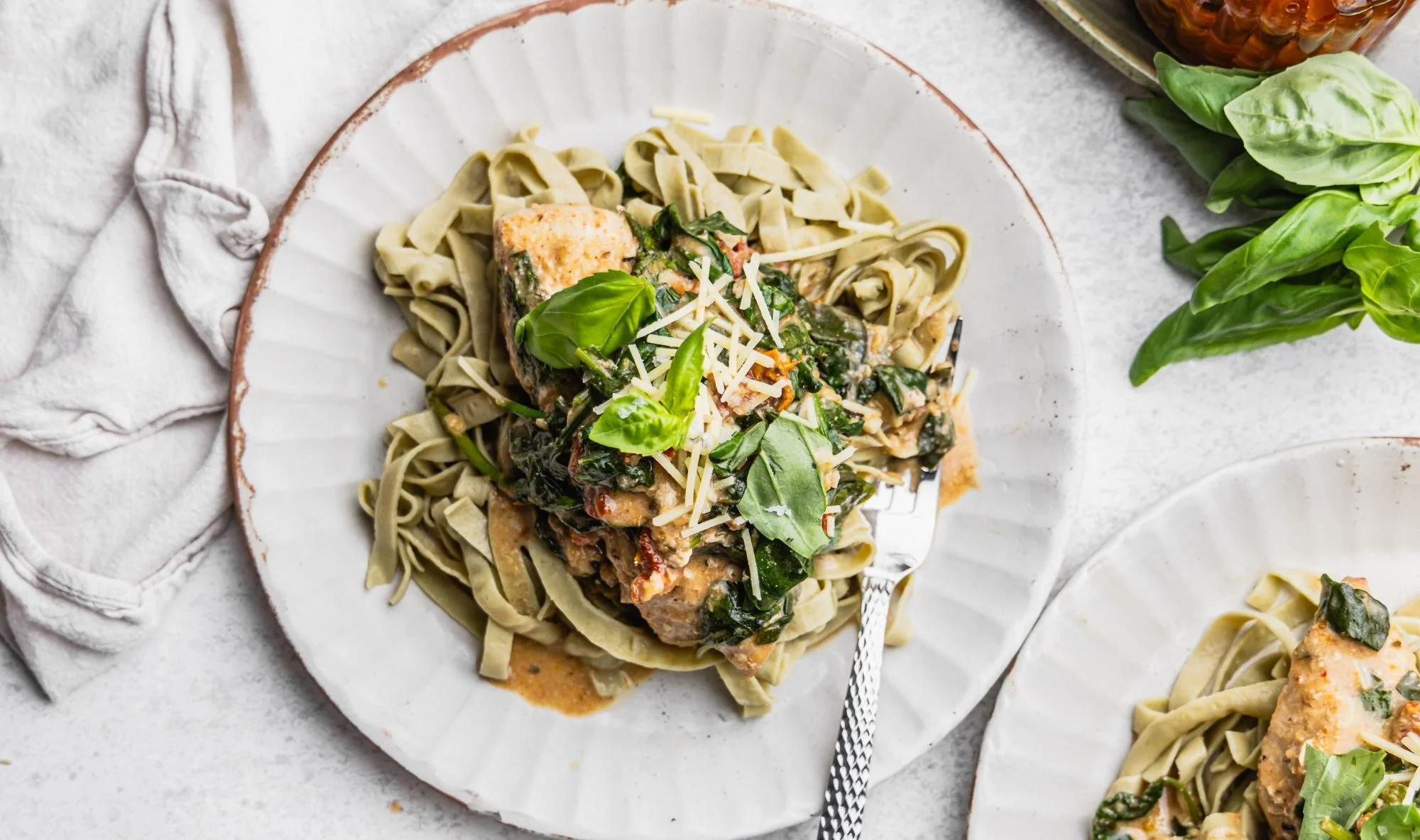 Slow Cooked Marry Me Chicken served over green edamame fettuccine with fresh basil and grated Parmesan on a white plate