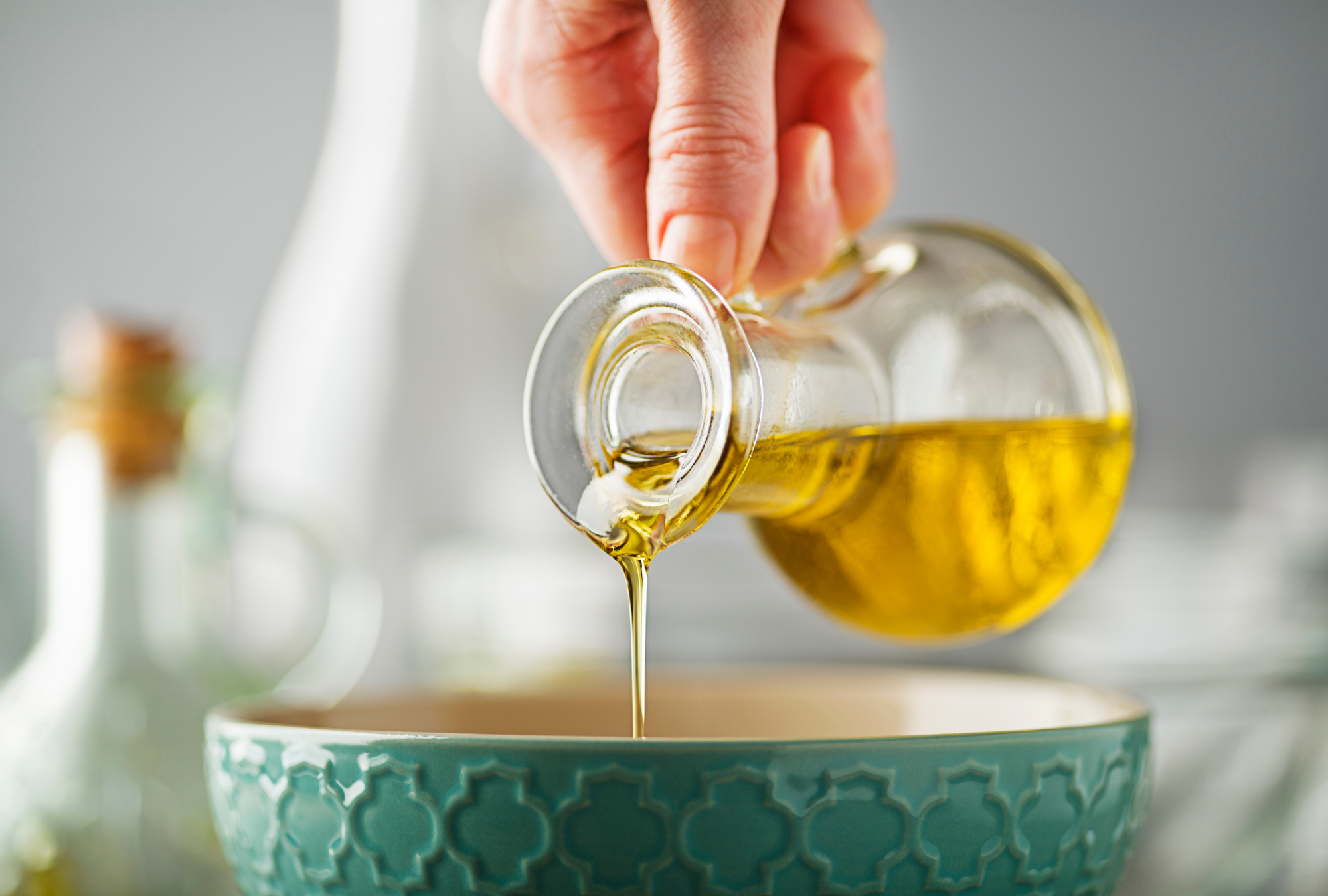 Close up of a hand pouring olive oil into a green bowl