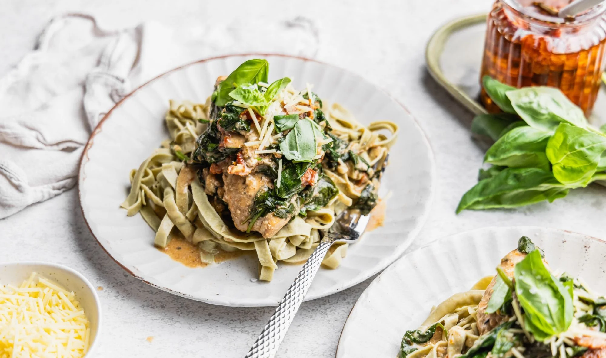Creamy slow cooked Marry Me Chicken with sun-dried tomatoes and wilted spinach over edamame pasta, topped with shaved Parmesan and fresh basil leaves