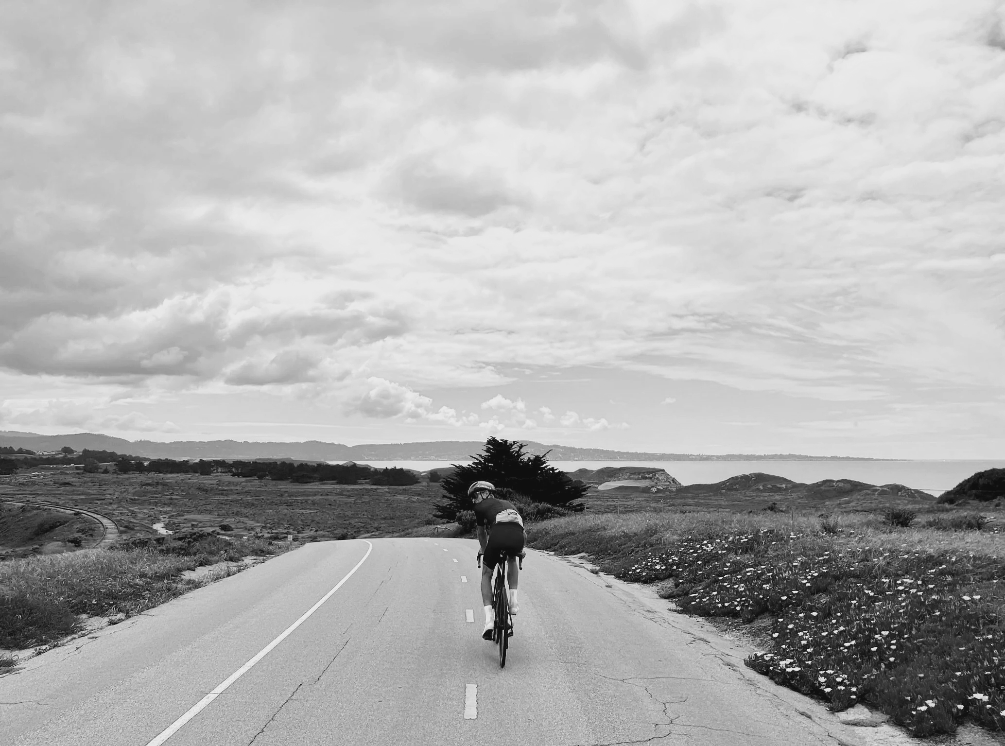 Cyclist on an open mountain road under dramatic skies — private guided riding with Santé