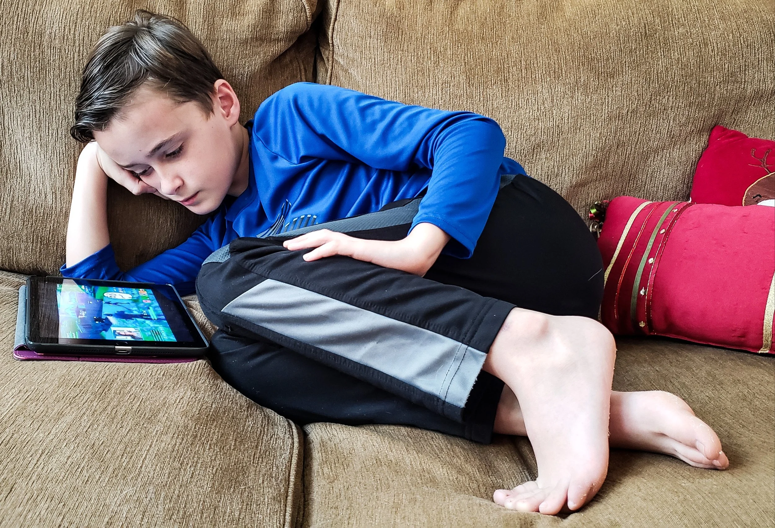 A young boy sitting on the couch using his tablet, representing how screen time and digital habits can influence children’s attention and cognitive development.