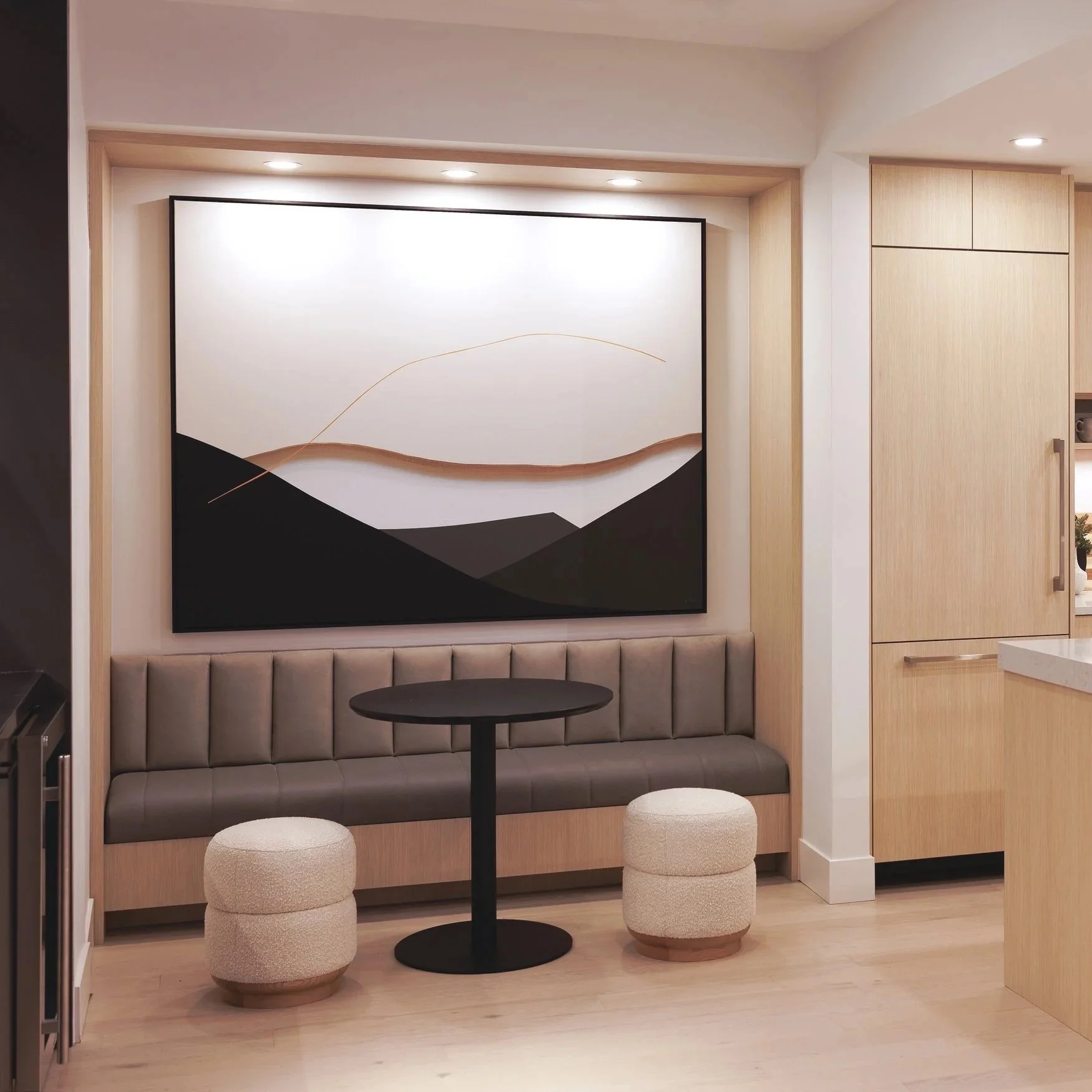 Amy Stewart abstract canvas print in a Modern dining nook with a beige upholstered banquette, two round ottomans, a small black round table, a large abstract black and white reproduction on the wall, and wood-paneled cabinetry in the background.