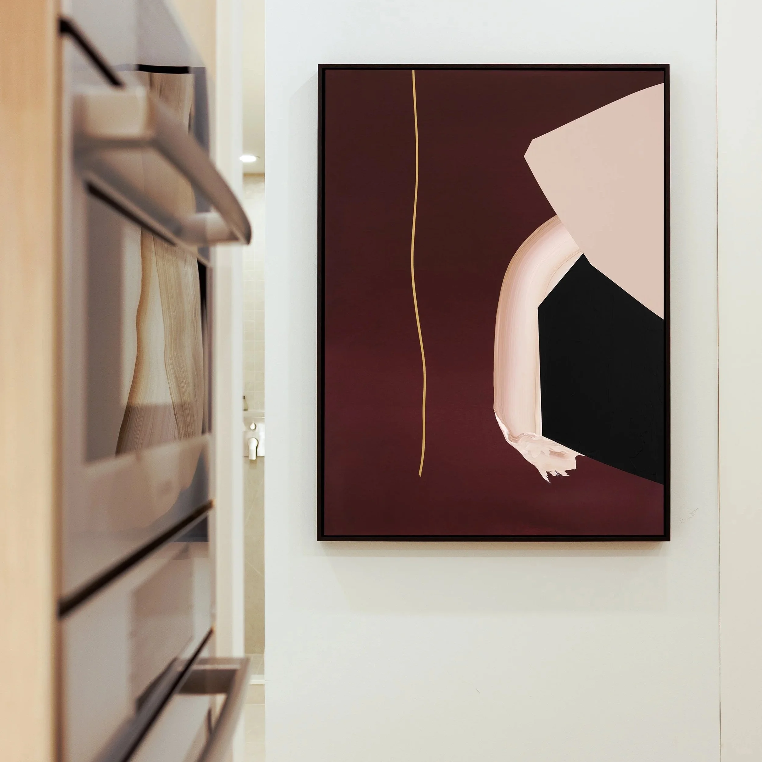 Amy Stewart abstract prints,  Abstract wall art with dark red background, a curved light pink shape, a dark black shape, and a thin yellow line on a white wall in a gallery.