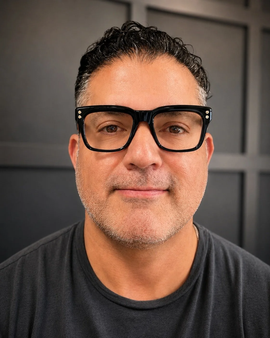 Close-up portrait of a man wearing black glasses with a dark background.