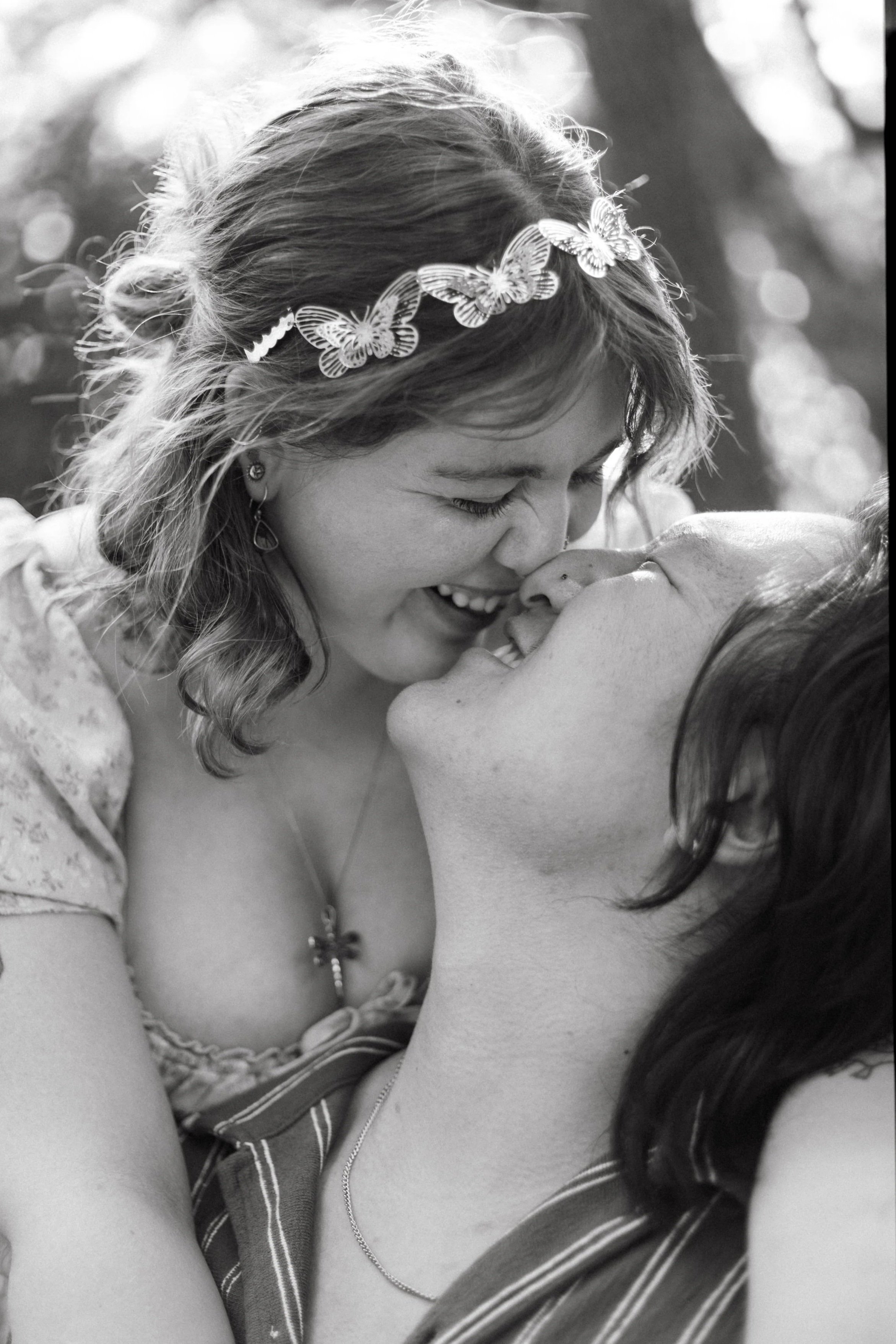 Two women are sharing a tender kiss, with one woman wearing a butterfly headband.