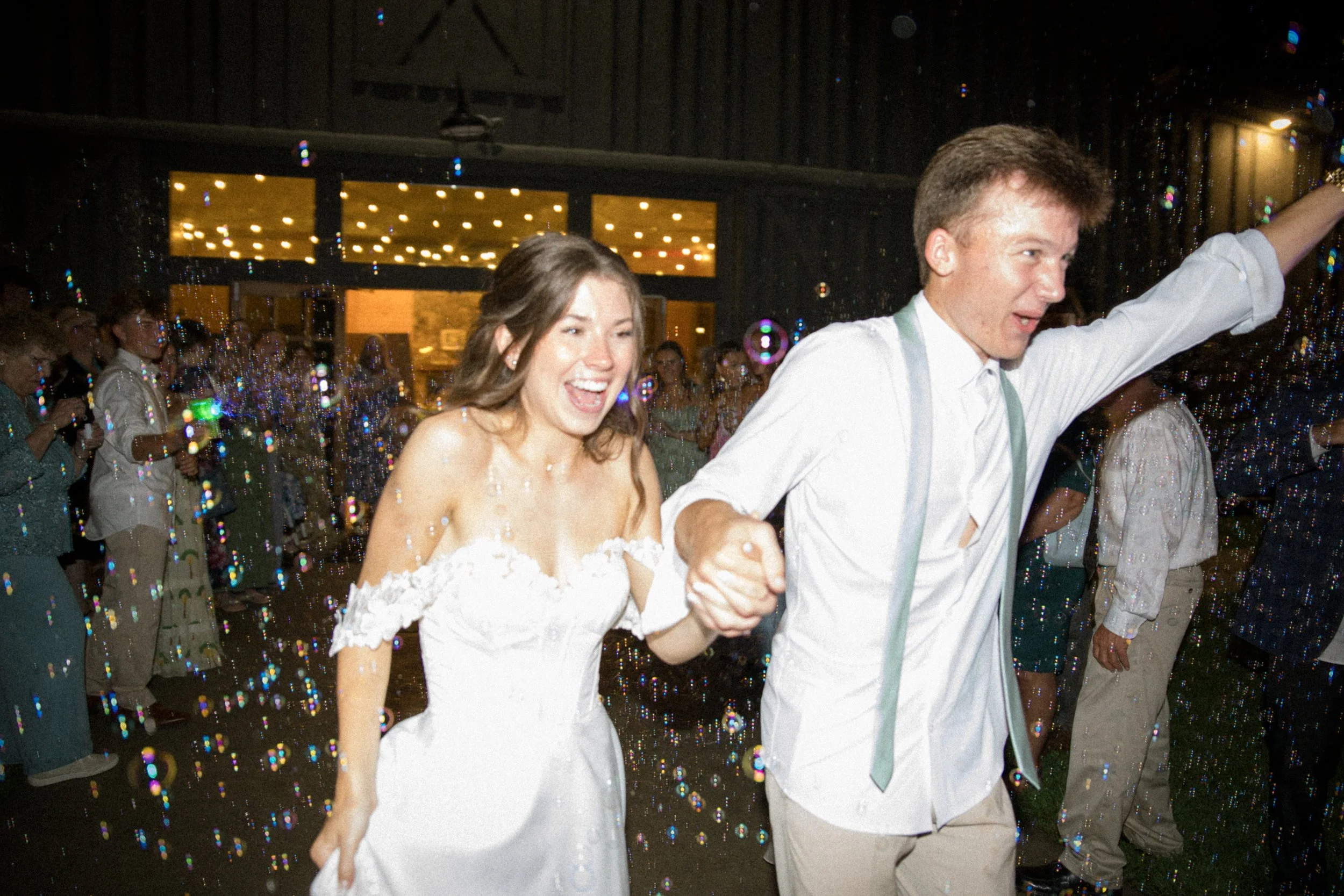 A happy bride and groom dancing together at their wedding reception, surrounded by guests, with colorful confetti and lights in the background.