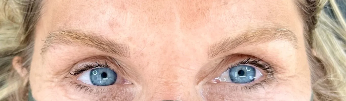 A woman with bright eyes modeling beautifully full and manicured eyebrows achieved through a cosmetic nano brow appointment. Jenn Fisk is expertly trained in both nano brows and microblading and will provide a natural result.