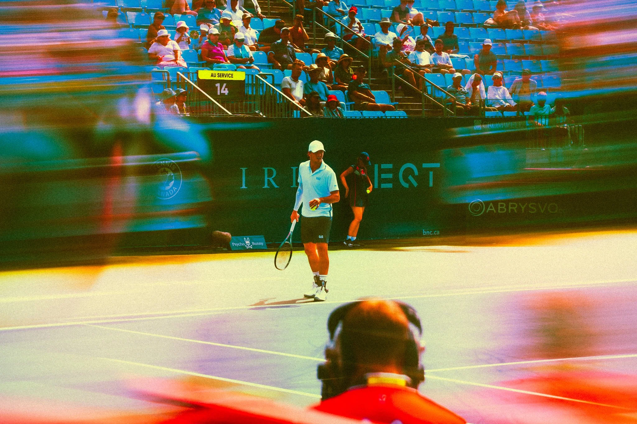 Un joueur de tennis marche sur le court tandis que d'autres personnes sont assises dans les gradins et regardent le match, avec une partie de l'image floue ou déformée.
Photographe sportif Montréal - Tennis Canada Ominium Banque 
