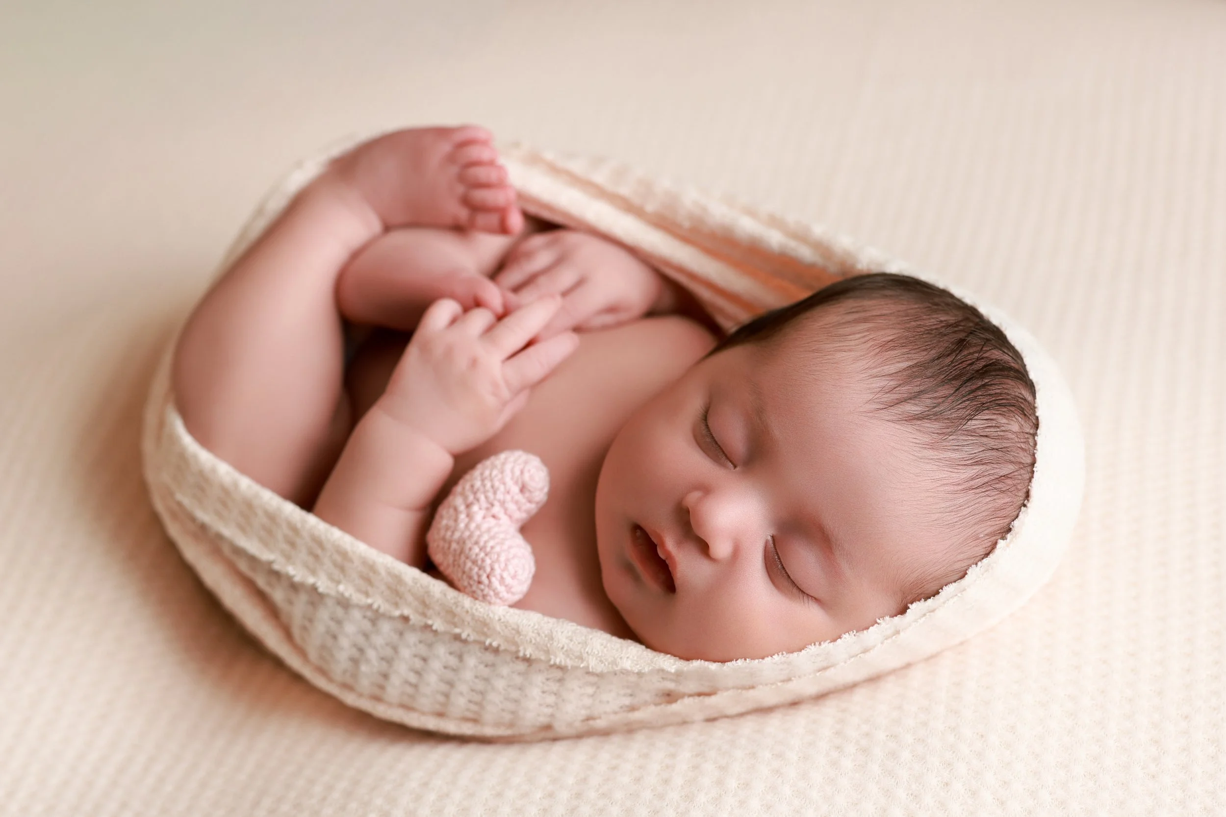 newborn baby girl wrapped on pink freebird shoppe fabric with tiny knitted heart