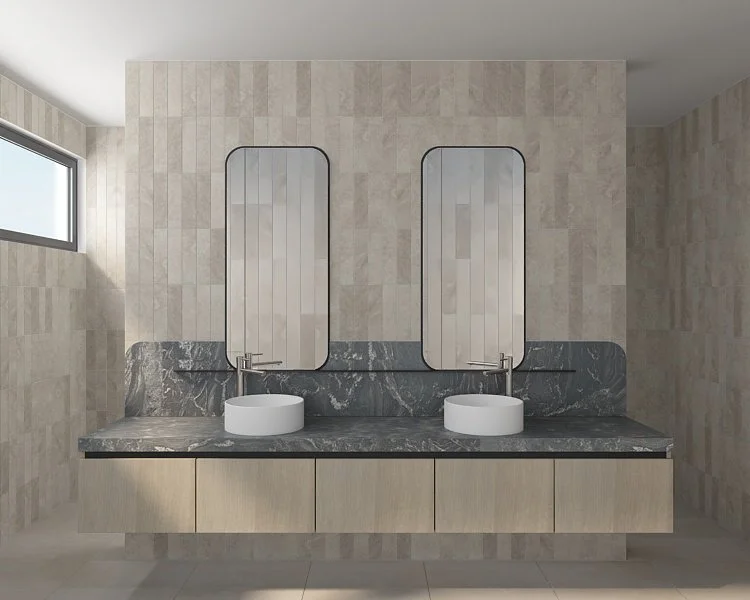 Modern bathroom with a double vanity, featuring two oval mirrors, two vessel sinks, and a dark gray marble countertop with a beige wooden cabinet below. Light-colored tiled walls and a small window to the left.