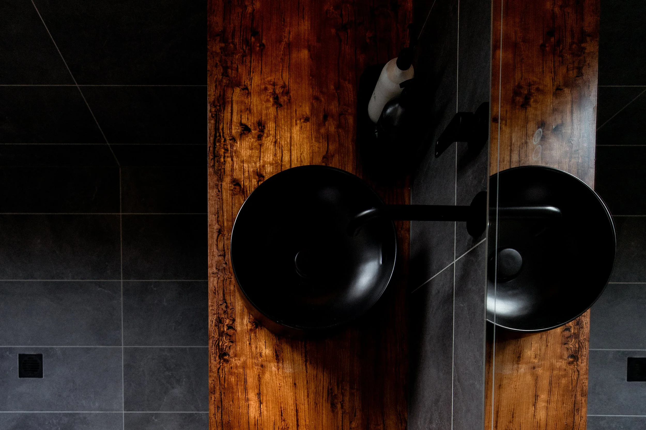 Black modern toilet bowl with a black toilet brush and dispenser on a wooden countertop in a bathroom.