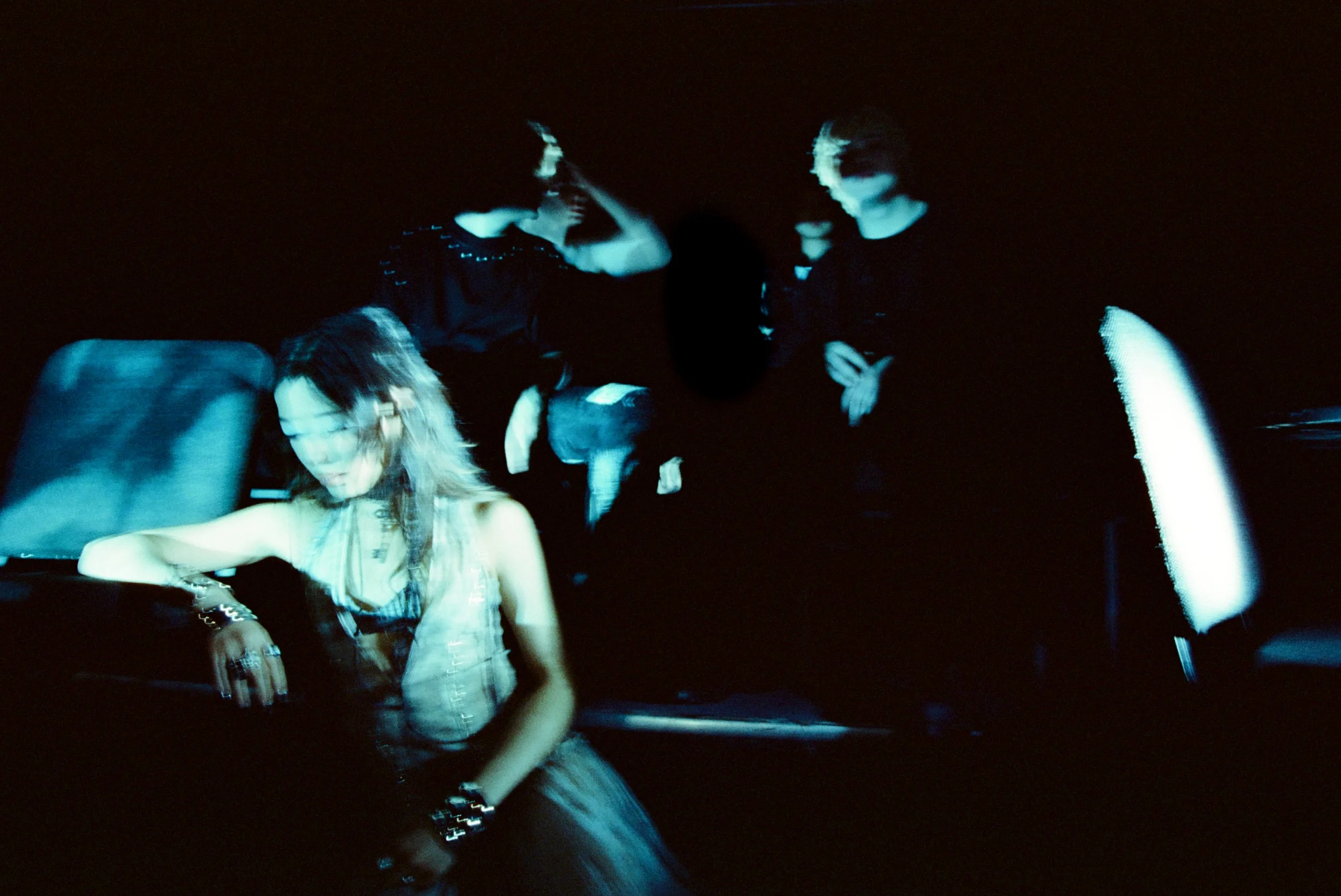 Blurry image of a woman looking off to the side with obscured figures behind her all bathed in blue light