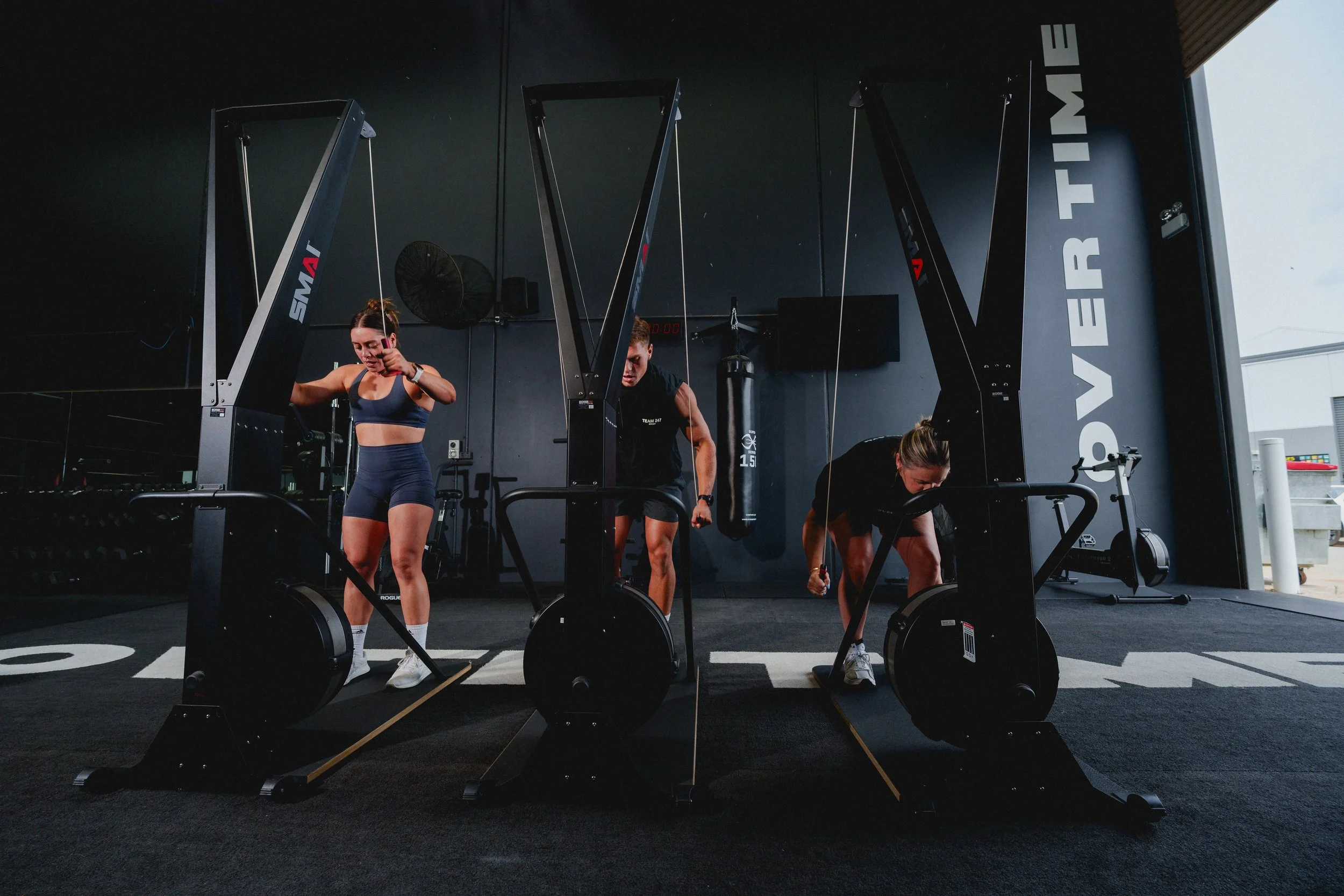 Three women exercising on rowing machines in a gym.