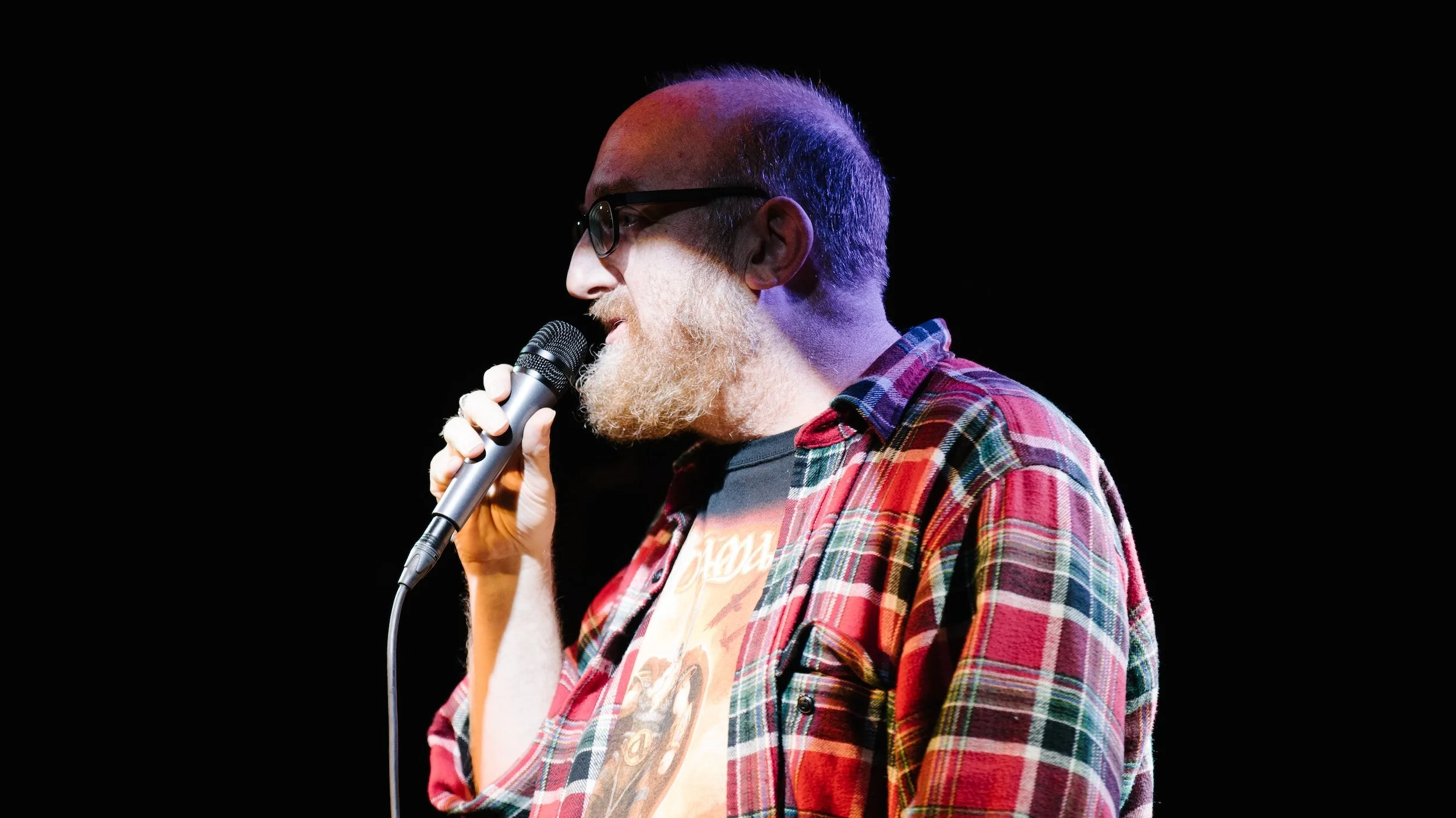 Comedian on stage, holding a microphone, delivering jokes to an engaged audience