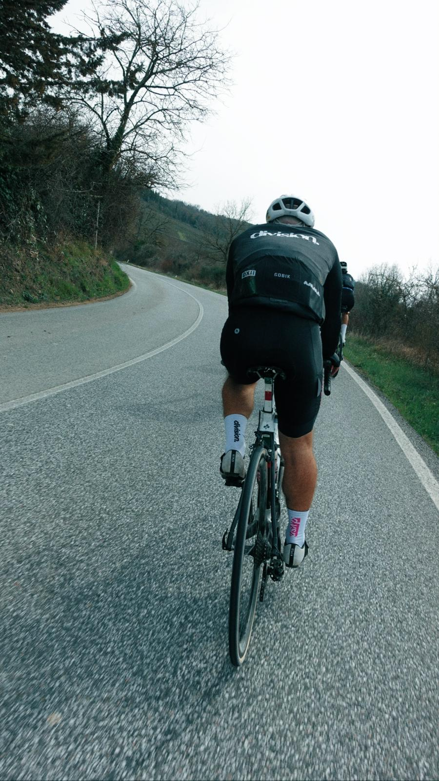 Ciclista pedalando em estrada curvada cercada por árvores e vegetação.