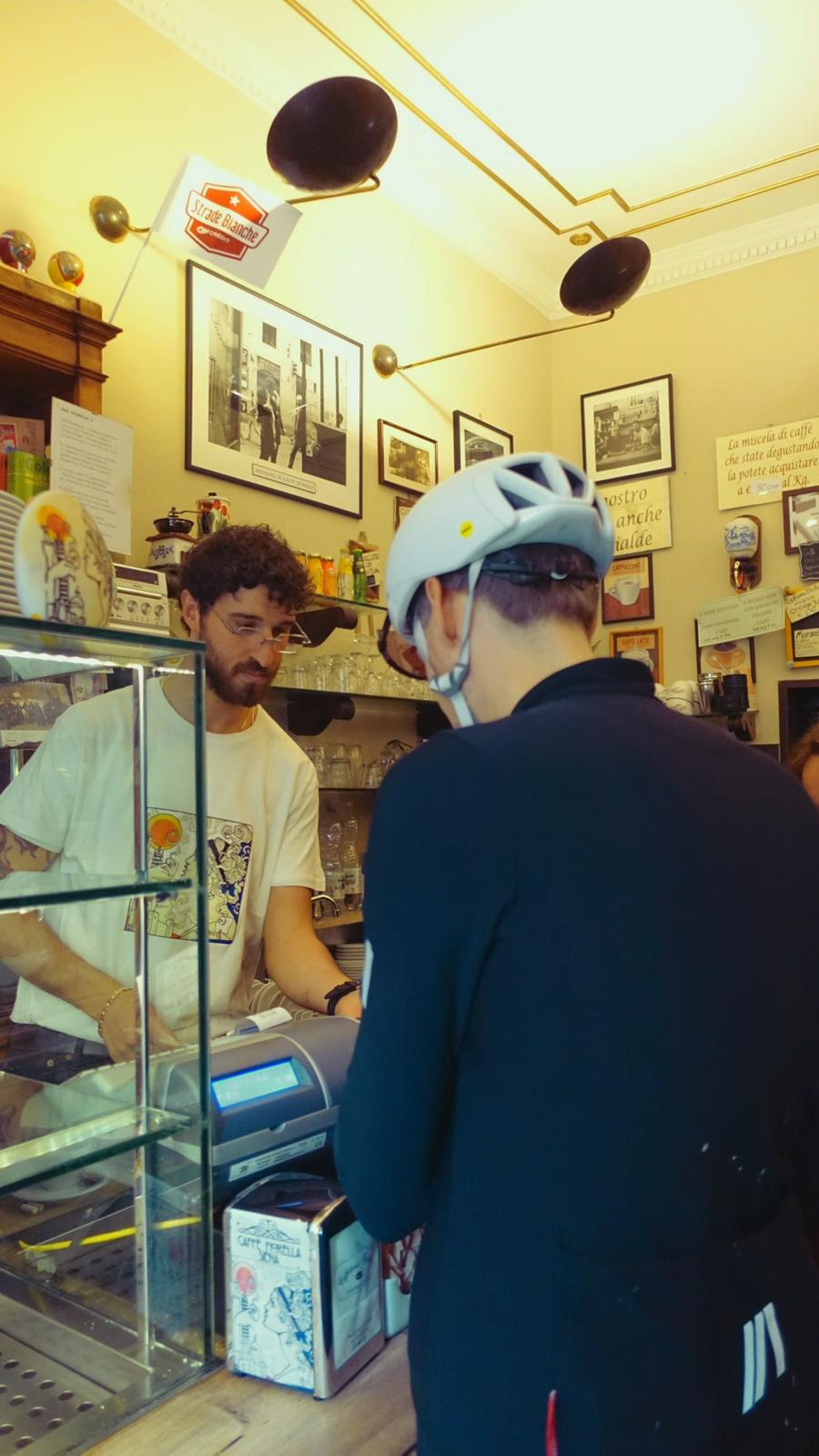 Homem com capacete de bicicleta faz Pedido em cafeteria italiana.