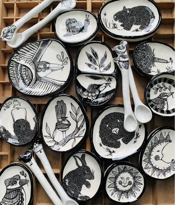 Collection of black and white animal-themed ceramic dishes and spoons on a wooden grid.