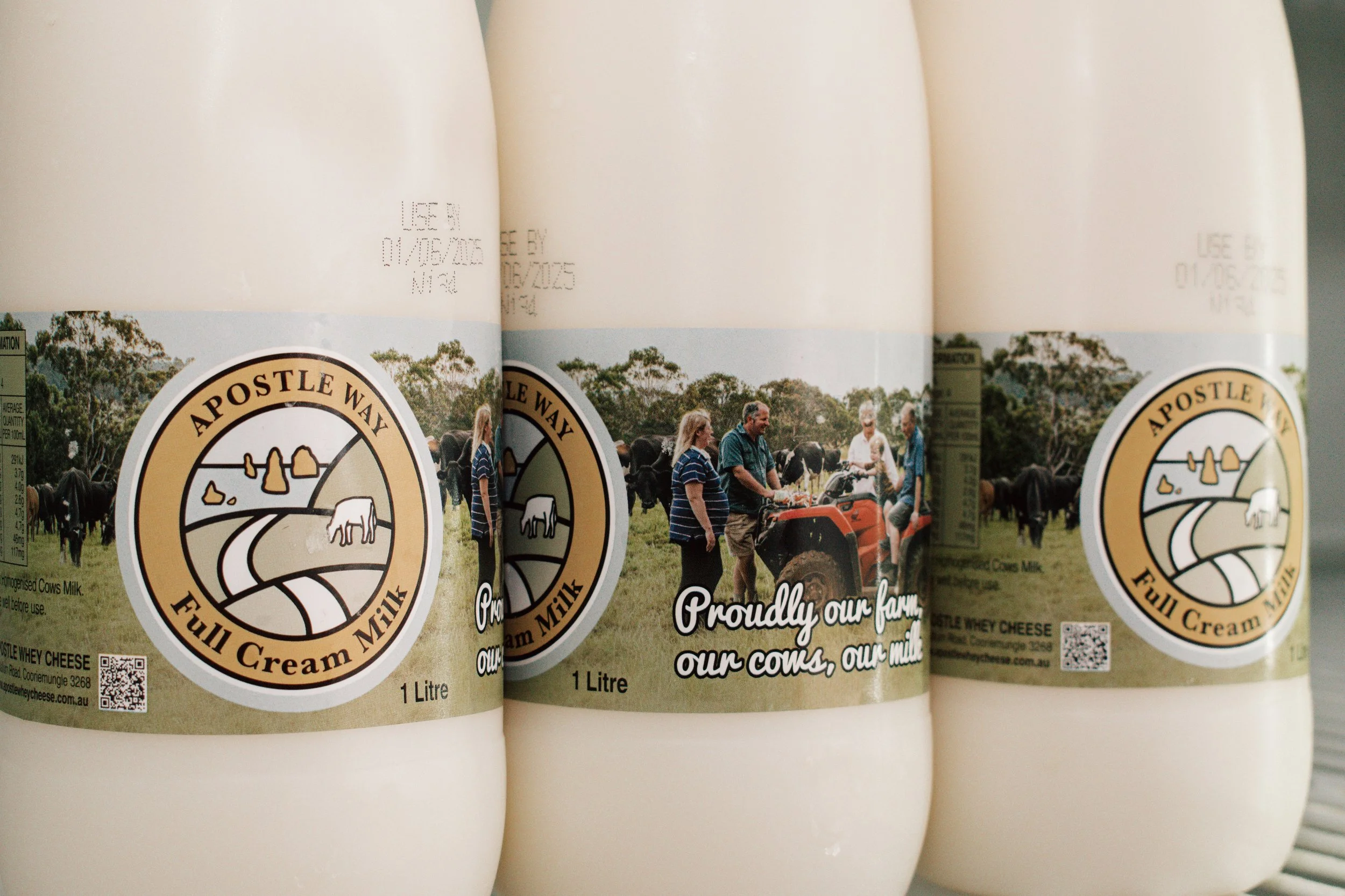 Bottles of full cream milk with a label featuring a logo of a farm scene and people in a field, with trees in the background.