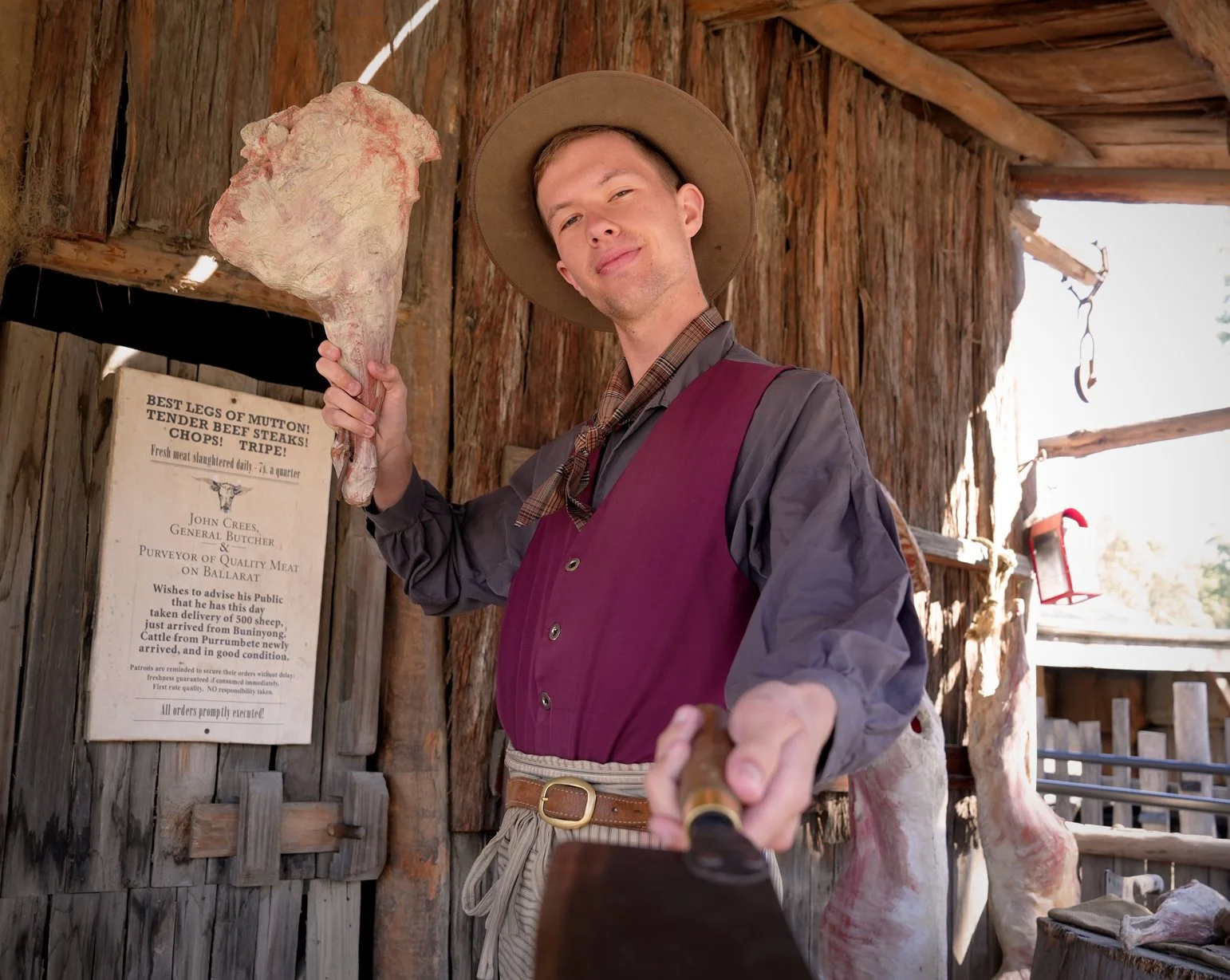 The butcher inside a his wooden structure with a cowhide and a sign in the background.