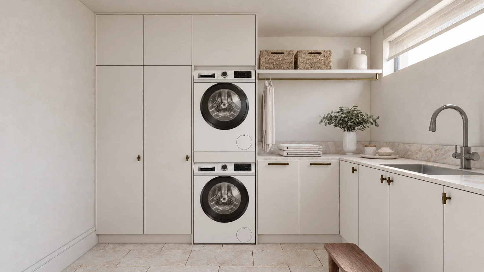 Laundry at P&O House with white cabinetry, a pale stone benchtop, brass handles and stacked appliances.