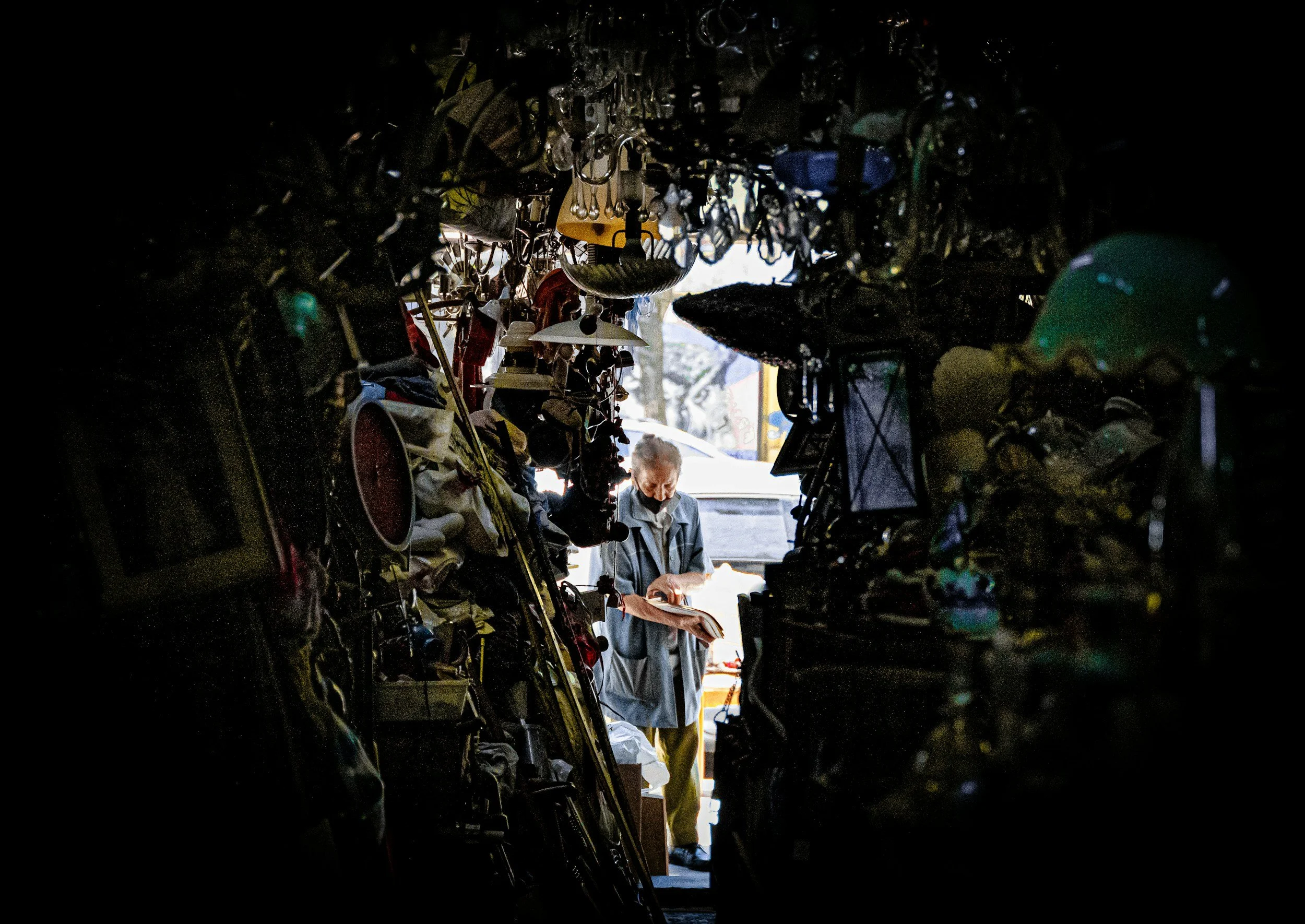 Large piles of clutter, lamps, clocks, and other debris frame a woman in her home.