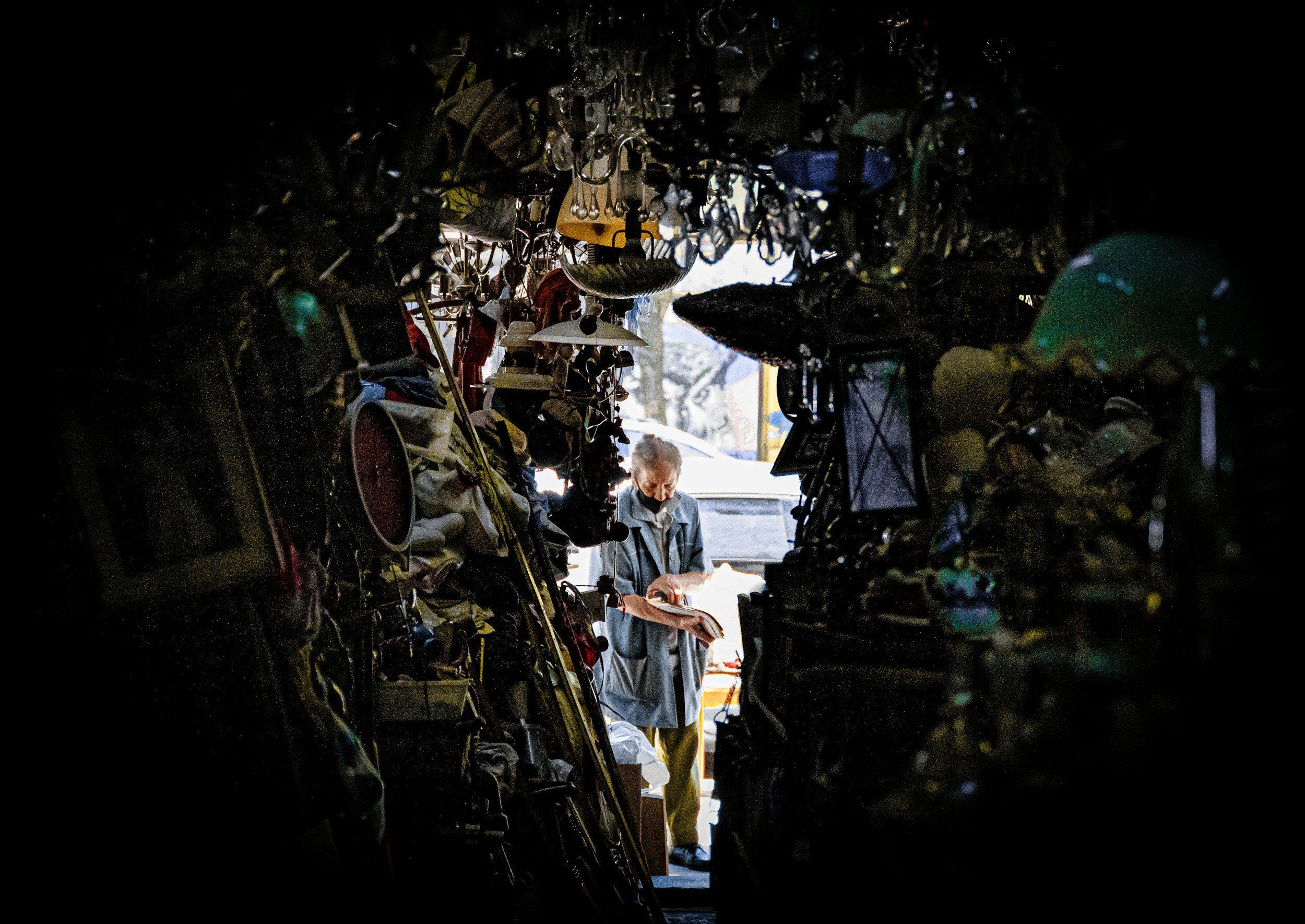 A woman is surrounded by clutter that is piled up to the ceiling in her home.