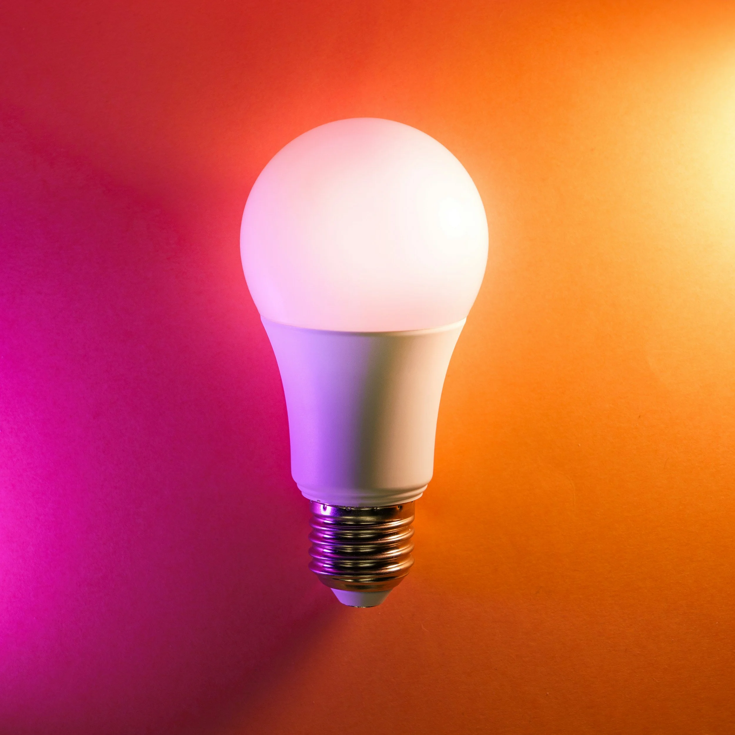 Close-up of an illuminated LED light bulb, glowing pink, against a vibrant orange background.