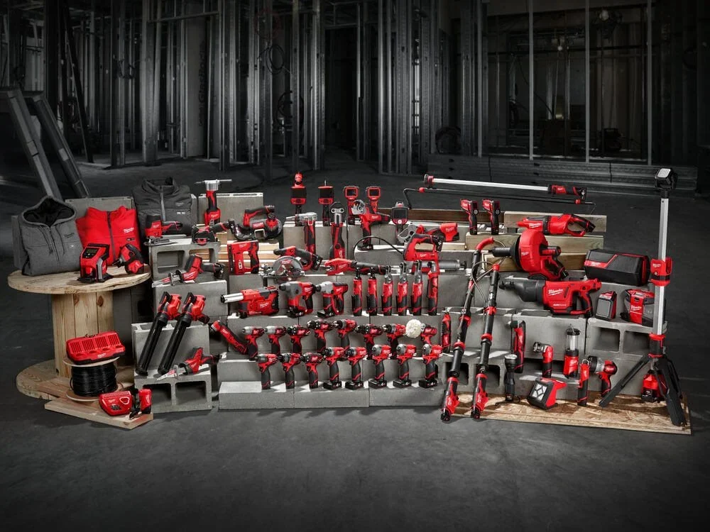 Array of red and black power tools and accessories arranged on cinder blocks and wooden platforms in a construction site