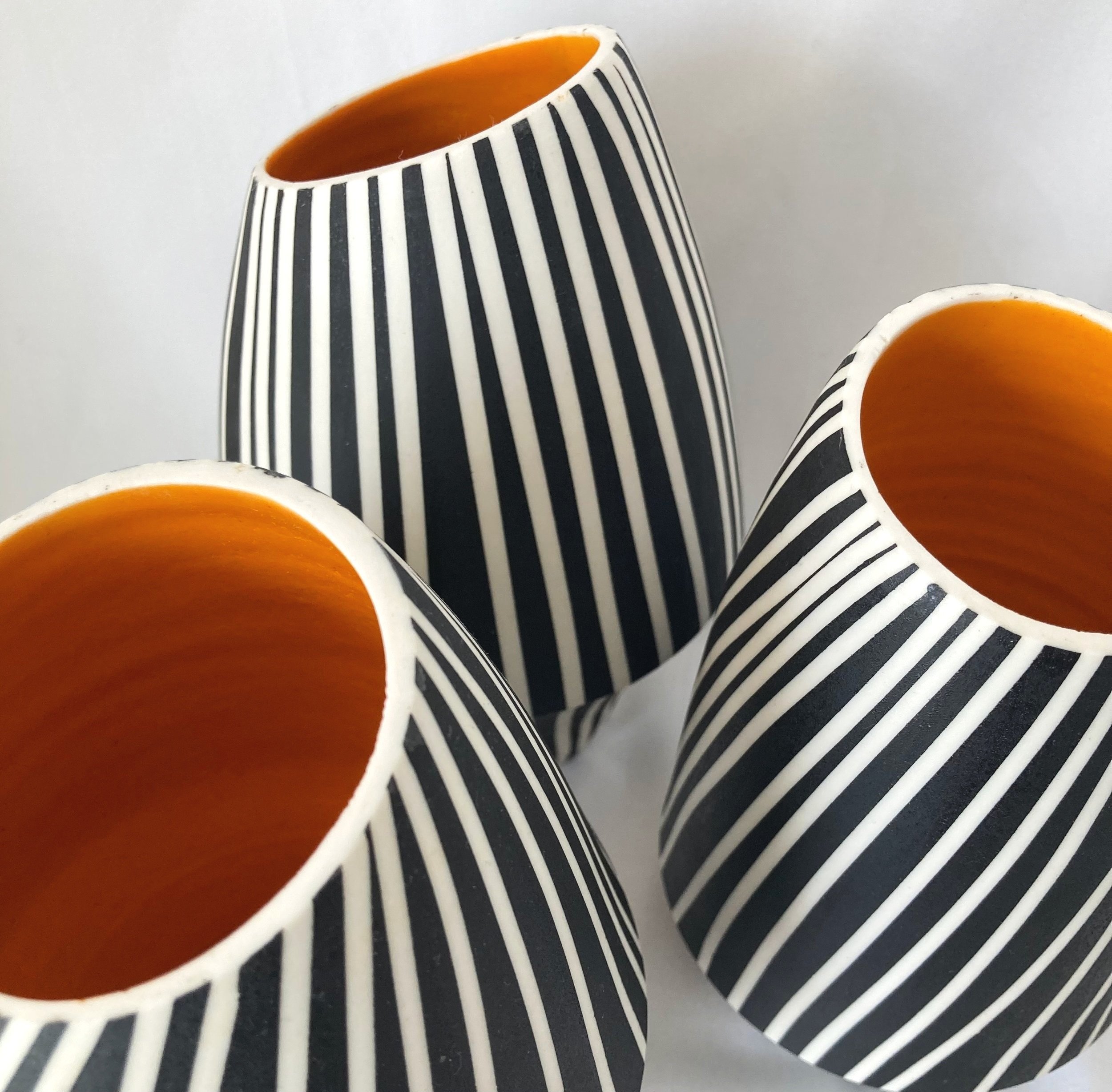 3 assymetric vases wheel thrown in porcelain with orange glazed interior and black and white striped exterior to create a sense of movement