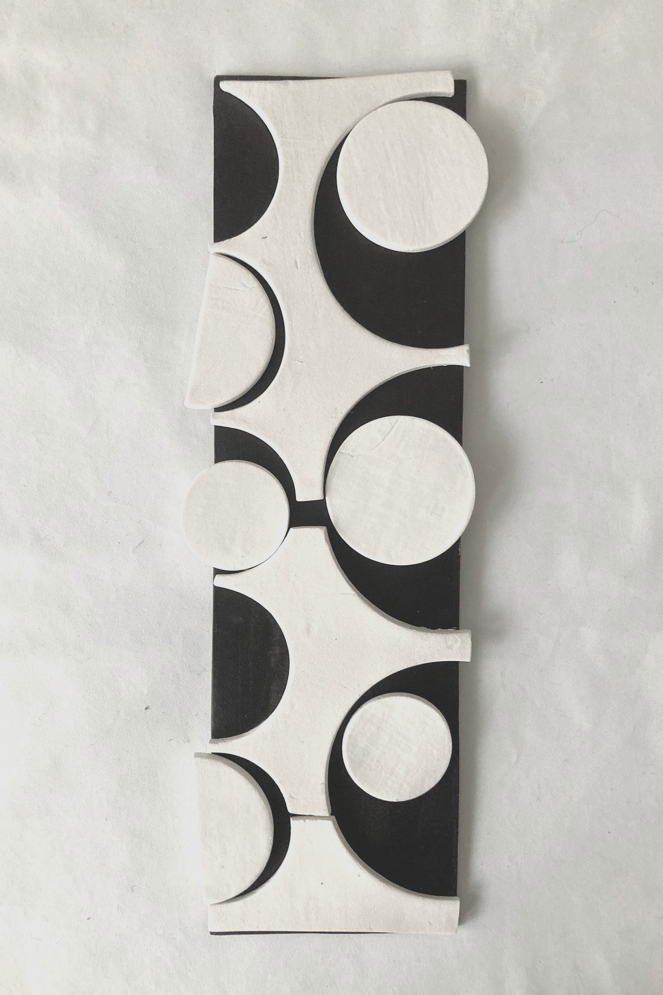 Rectangular porcelain wall panel with black ground and collaged porcelain positive and negative shapes to create a sense of shifting movement