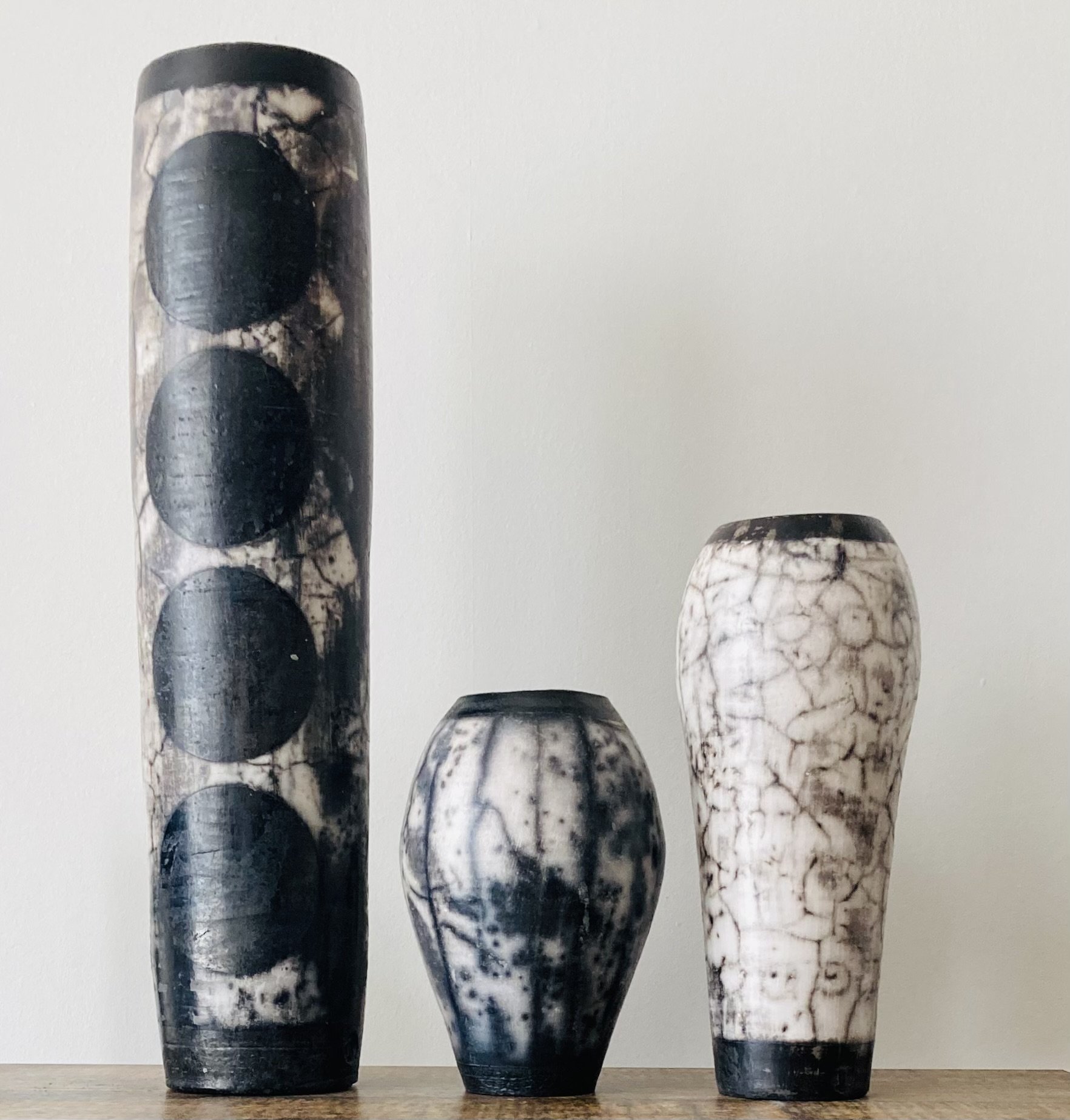 3 naked raku vases in black and white; a tall one with large spots, a small one with stripes and a medium one showing crackle