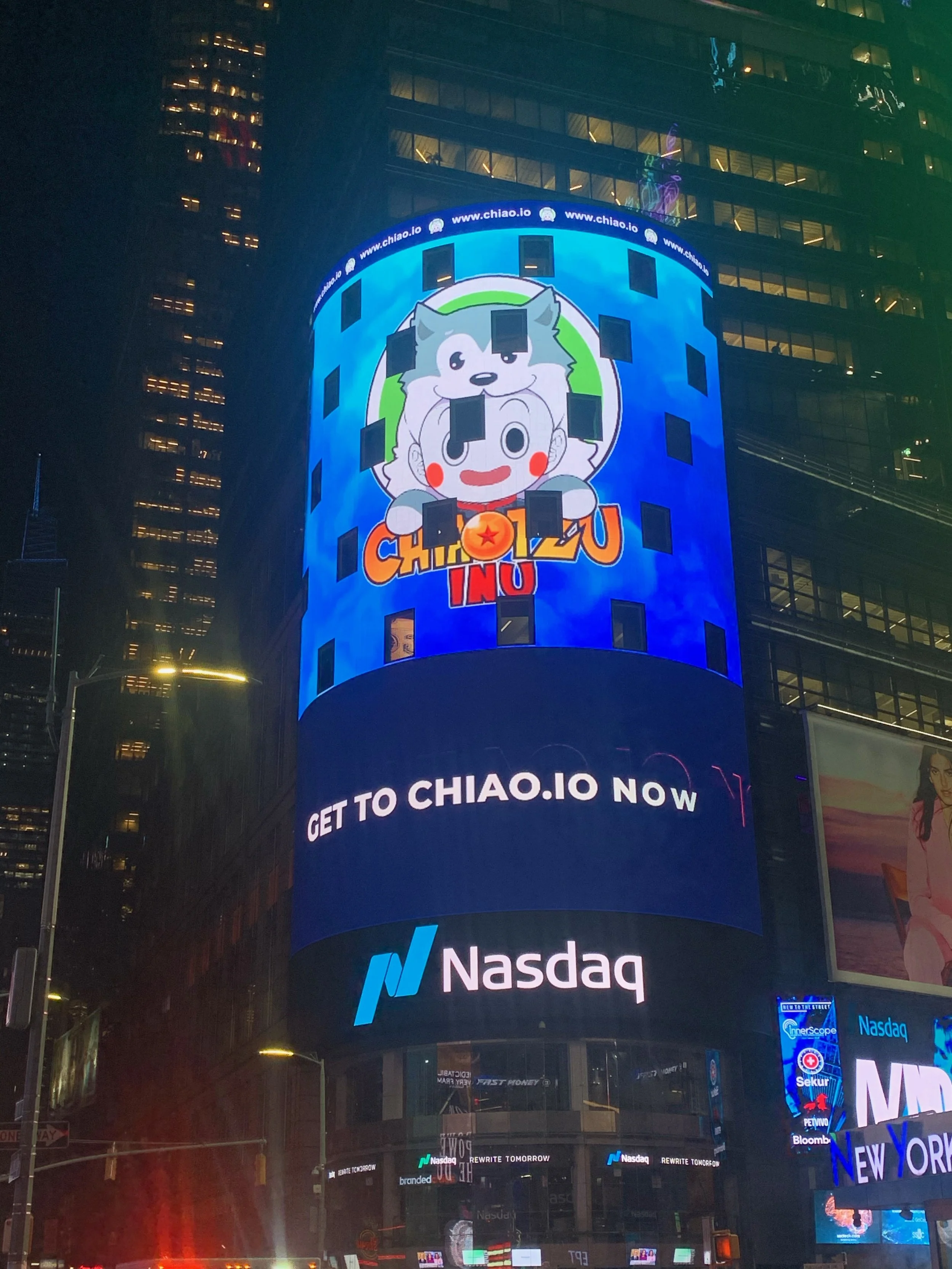 Nighttime view of Times Square with digital billboards, including logos for Nasdaq and Chiao.io, and a large cartoon character with the words 'Chiao.io' and 'Get to Chiao.io now' displayed.