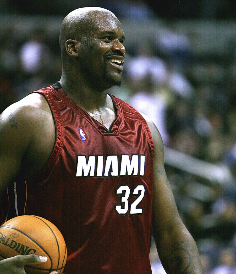A basketball player wearing a Miami jersey with the number 32, smiling and holding a basketball on a court.