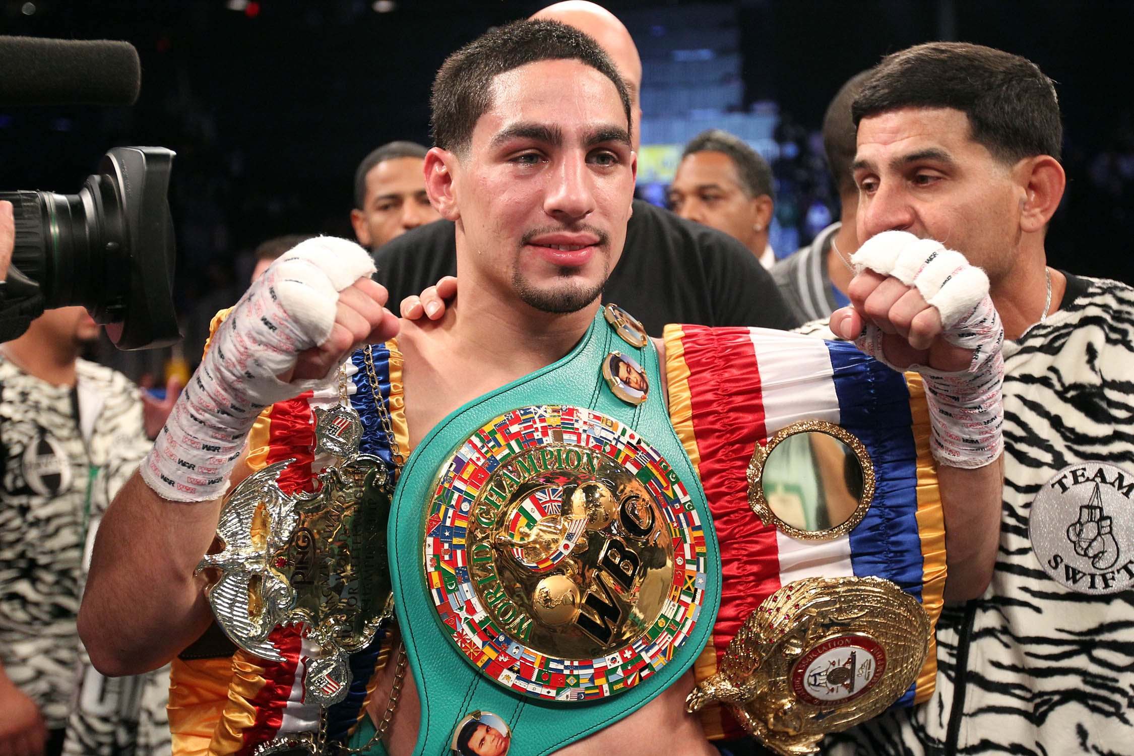 Professional boxer wearing multiple championship belts and medals, celebrating victory in the ring, with a focus on his determined face and the accolades displayed.