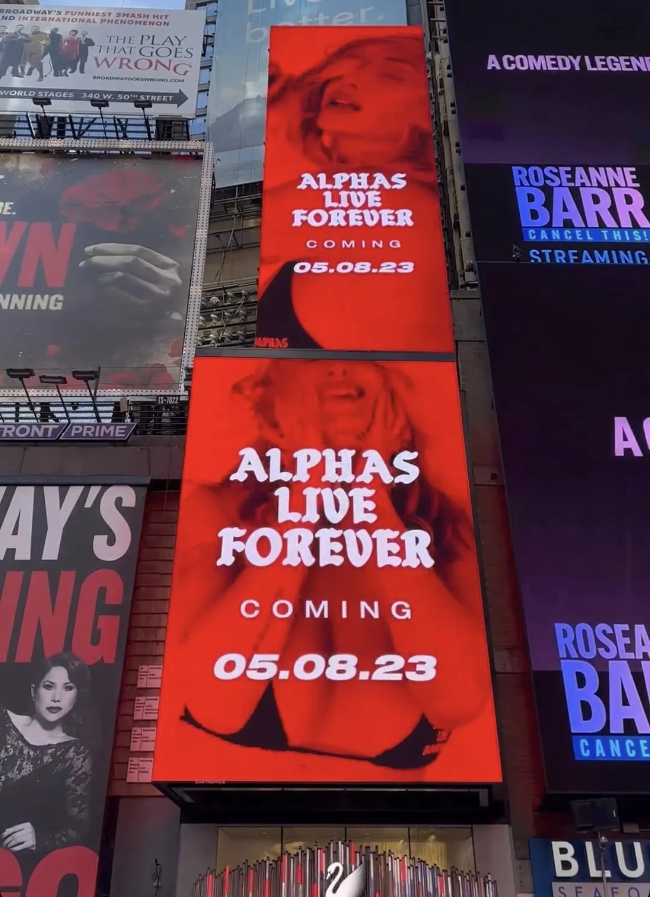 Bright red digital billboard advertising a show titled "Alphas Live Forever," coming on August 5, 2023. The billboard features an abstract, red-tinted image of a smiling woman and includes a silhouette of a woman with long hair and a bikini top at the bottom.