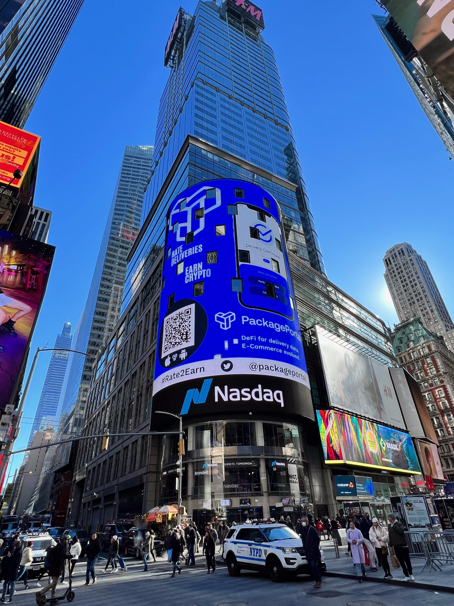 Times Square in New York City with digital billboards, a crowd of pedestrians, several NYPD vehicles, and tall buildings.