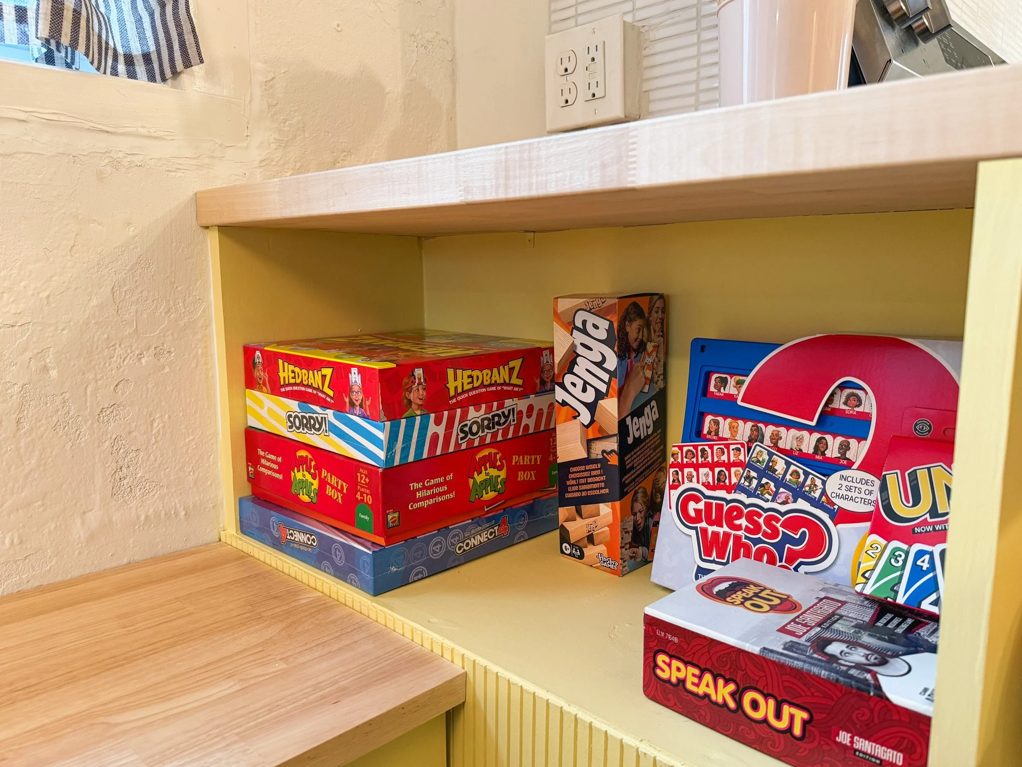 A yellow shelf holding several board games including Hedbanz, Sorry, Jenga, Guess Who, Connect 4, and Speak Out.
