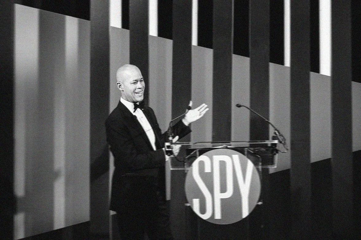 Black and white photo of Vlad Duthries speaking behind an on-stage podium that says SPY at the International Spy Museum's Hidden Hero Awards.