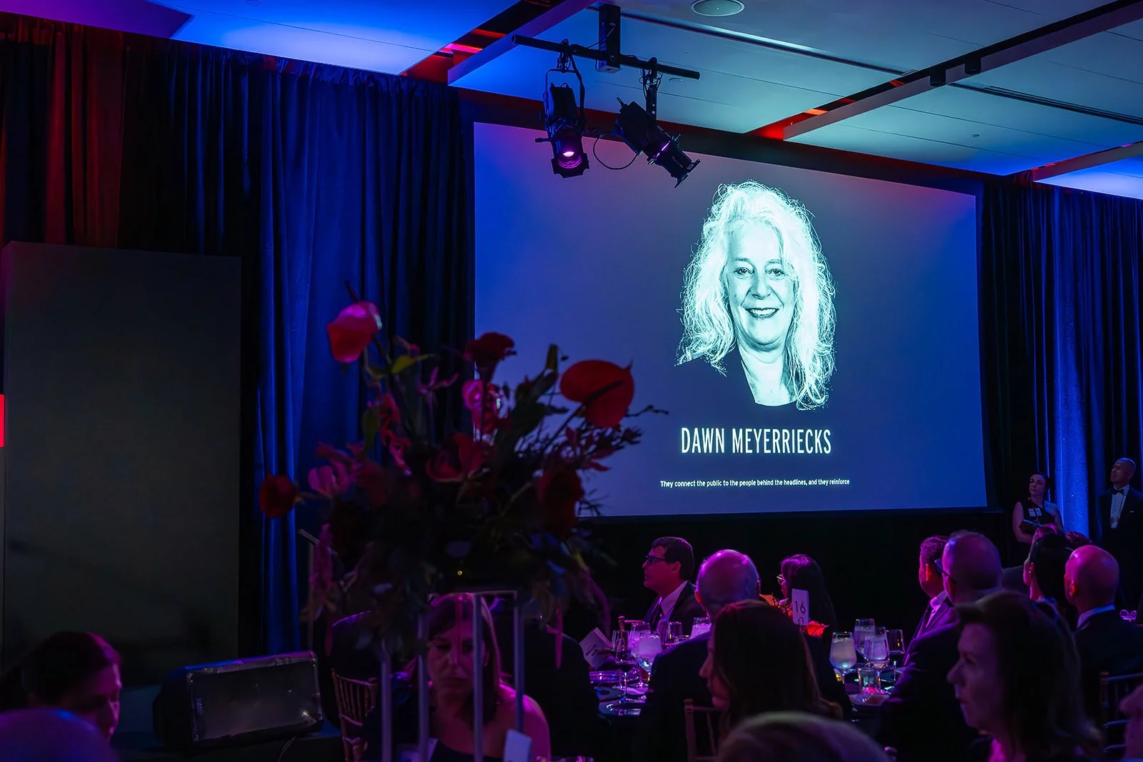 A video featuring Dawn Meyerriecks plays on a large screen in the event ballroom.