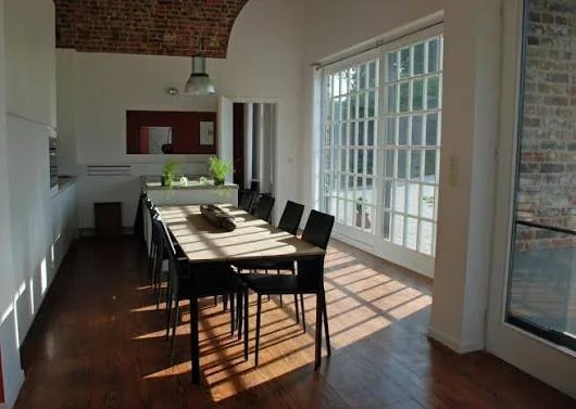 Eethoek in een lichte kamer met grote ramen en houten vloer.