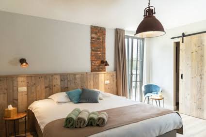 Slaapkamer met houten accentmuur, bed met badstof handdoeken, een nachtkastje en een stoel bij het raam.