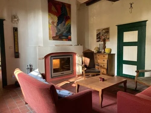 Gezellig woonkamer met een open haard, houten tafel, roze bank en stoel, groene deur, en muurdecoraties.