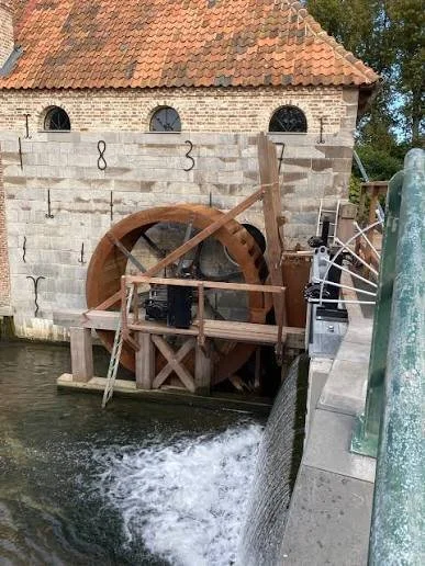 Uitzicht op de watermolen van Erfgoedlogies Metstermolen met waterwiel en water dat er doorheen stroomt.