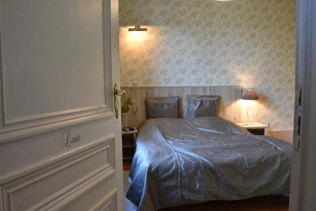 Een slaapkamer met een bed, twee hoofdkussens, een nachtkastje met een lamp, een muur met bloemenbehang en zacht verlichte verlichting.