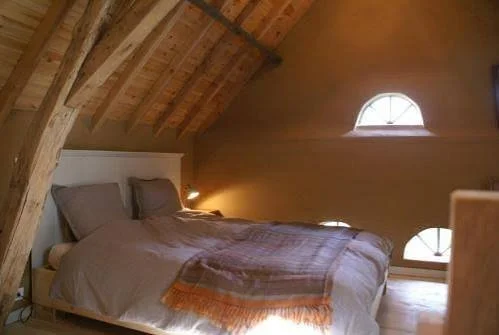 Slaapkamer met een bed, houten plafond en twee kleine, ronde ramen
