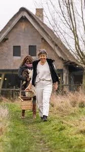 De uitbaters van Hoeve Corfs in Wellen wandelen samen voor een landelijke boerderij terwijl ze een mand dragen.