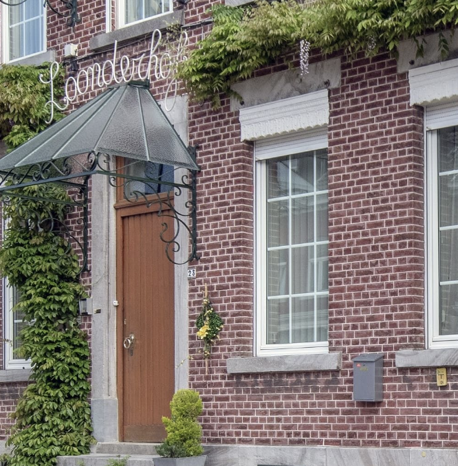 Een rode bakstenen gevel van B&B Het Loonderhof met een houten voordeur, grote ramen met witte kozijnen, groene klimplanten.