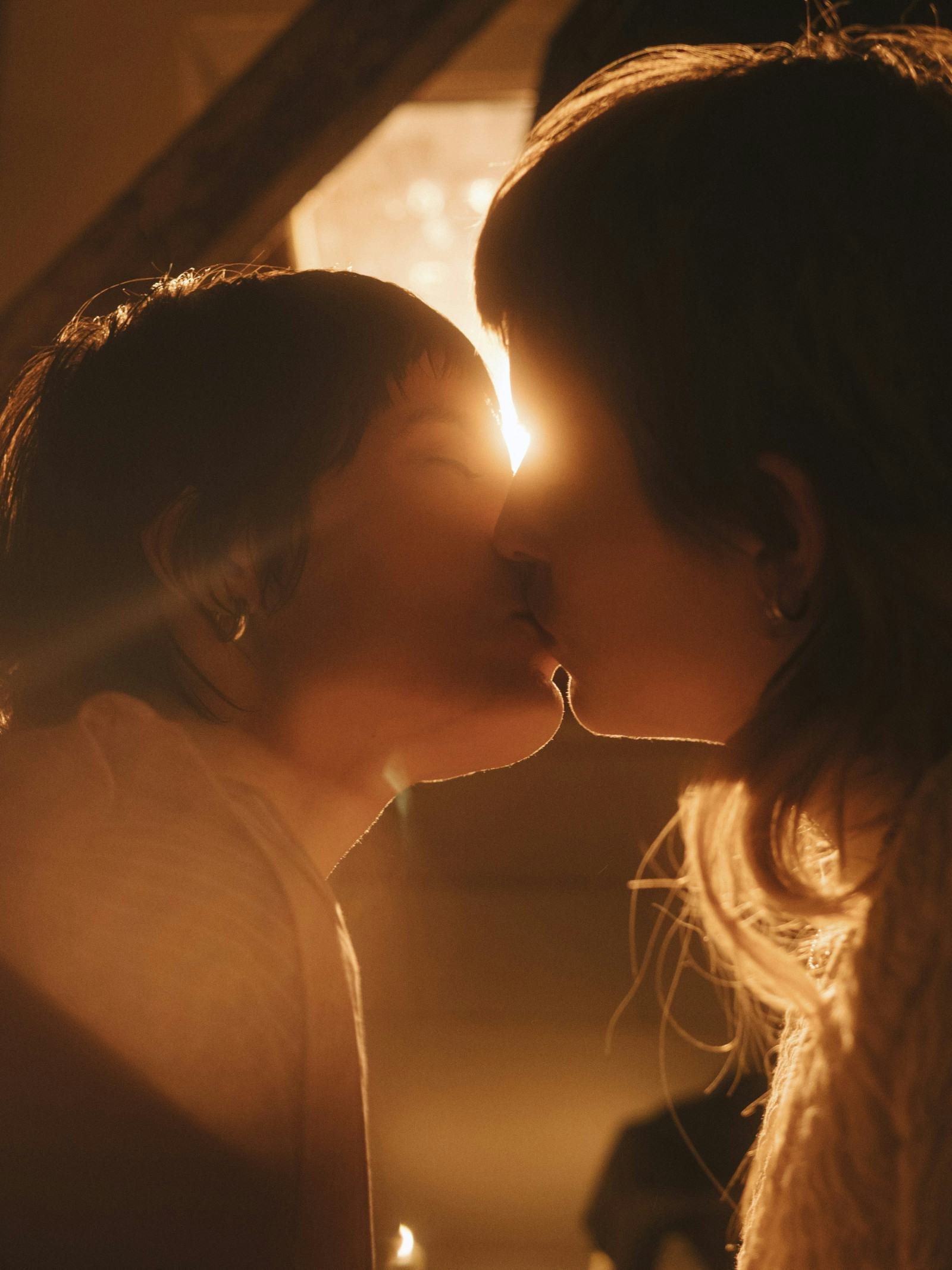 Silhouettes of a couple with foreheads touching, backlit by warm, golden light, creating a romantic and intimate scene.